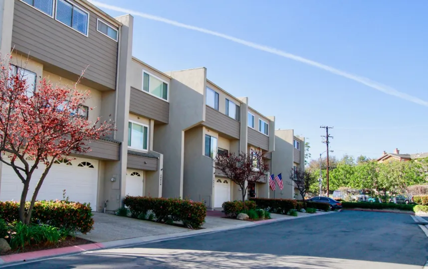 Row of Village Court apartments with garages and bushes on a sunny day.