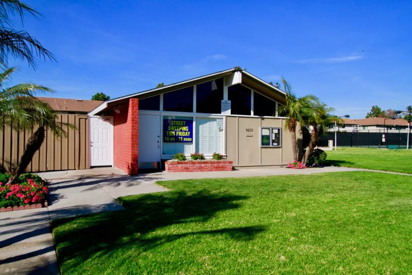 Village Townhomes building with a sidewalk and palm trees on a sunny day.