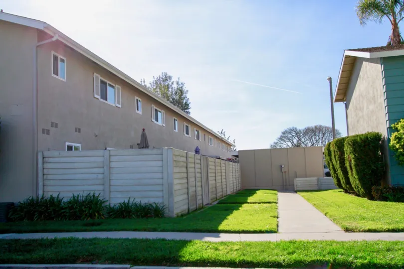 A sunny day in the Village Townhomes with row houses, trees, plants and lawn.