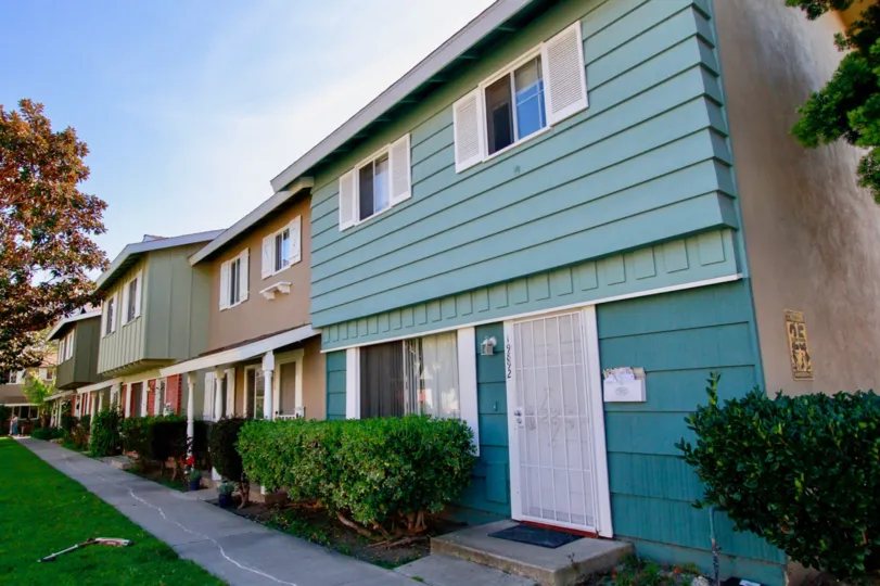 Row of Village Townhomes with a sidewalk and trimmed bushes.