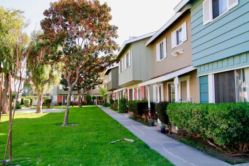 Row of Village Townhomes with a sidewalk and trimmed bushes.