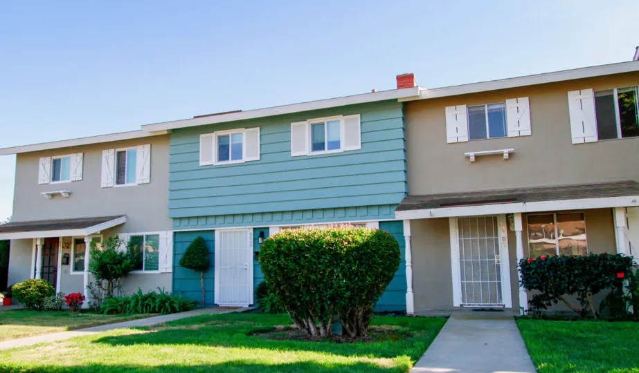 Row of Village Townhomes with a sidewalk and trimmed bushes.