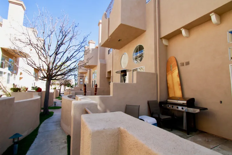 Sidewalk between Villas at Huntington Beach buildings with a grill and deck chairs.
