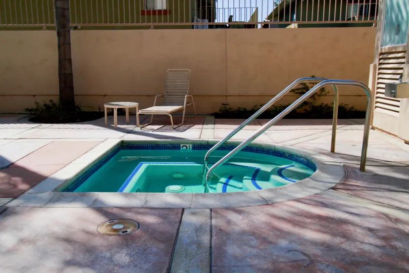A SWIMMING POOL WITH THE RAMP AND A SITTING CHAIR WITH TABLE ALSO AVAILABLE AND A TREE ALSO NEAR TO THE HOUSE THAT LOCATED NEAR TO THE POOL.