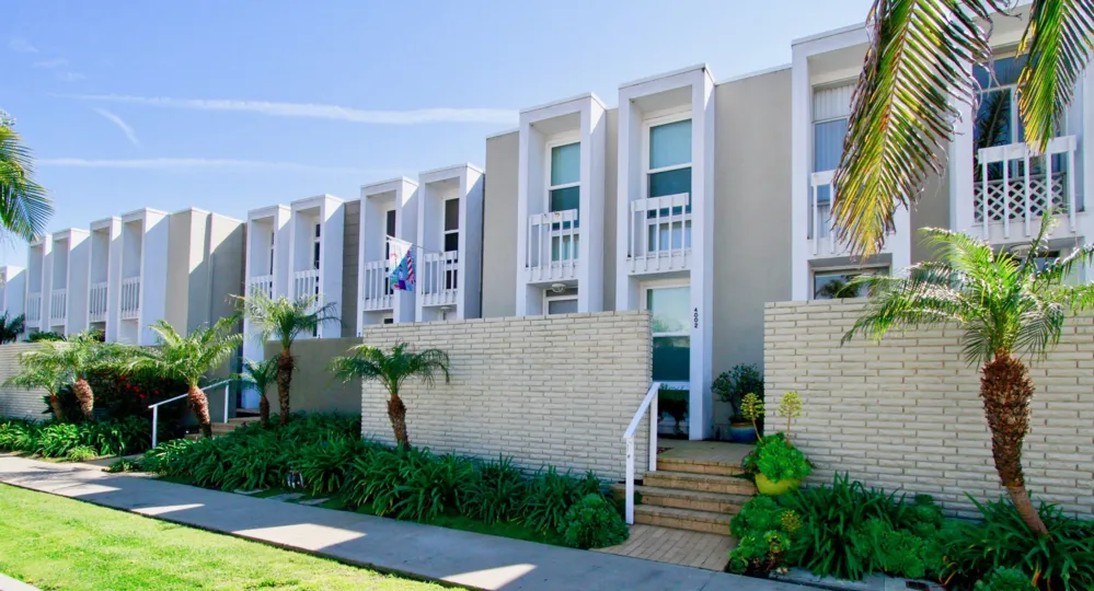 THE APARTMENTS ARE LOOKING BEAUTIFUL WITH WHITE COLOUR AND A SMALL ROAD NEAR TO THE PLACE AND TREES AND PLANTS ALSO NEAR TO THE APARTMENTS.
