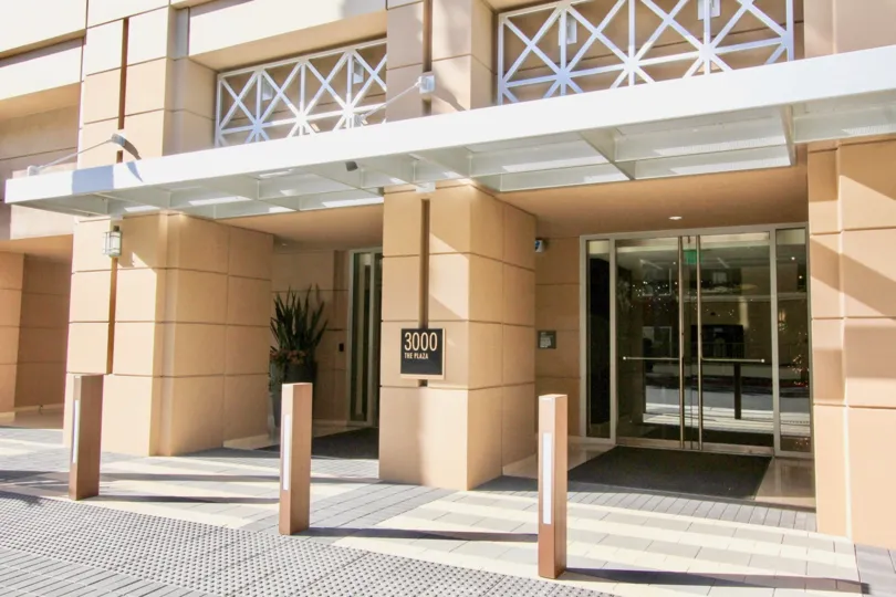 A large glass entryway leading into a large residential building at 3000 The Plaza in Irvine CA