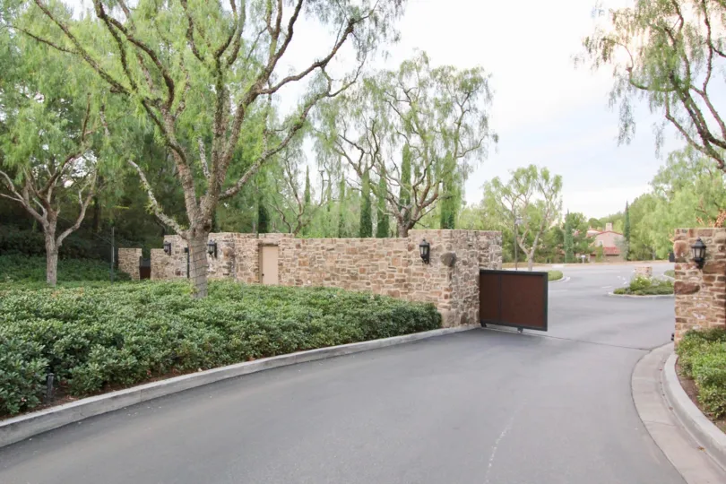 A cloudy day in Chantory with a security gate and tall trees and hedges.