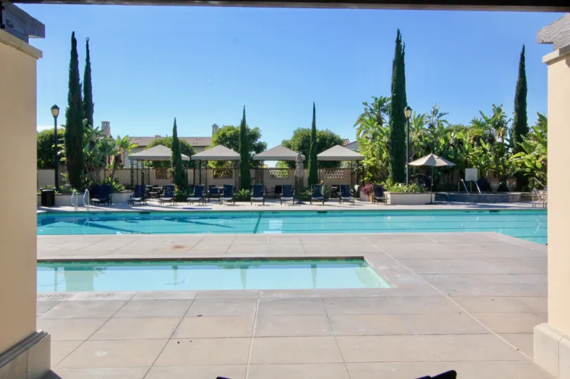 A clean pool decorated with chairs inside the compound with sheds near building decorated with trees and plants in Coronado