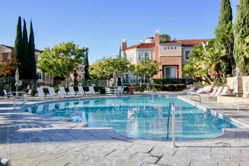 THE SWIMMINGPOOL WITH LOT OF CHAIRS, SURROUNDED BY PLANTS AND TREES, VILLA IS THERE IN THE IRVINE CITY
