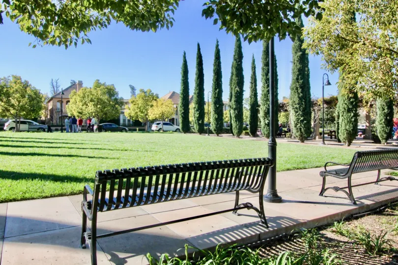 A sunny day in Cortile with a park with cypress trees and benches on a sidewalk