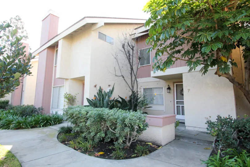 A two story pink and white building with a sidewalk and hedges inside Deerfield townhomes in Irvine CA