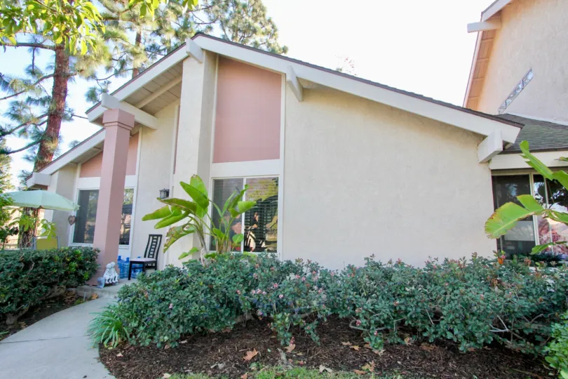A sunny day in Deerfield Townhomes with a modern house with pale pink plaster, surrounded by tall trees.