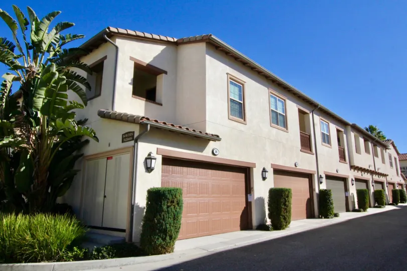 A sunny day in Four Quarters with houses with garages, blue sky and hedges.