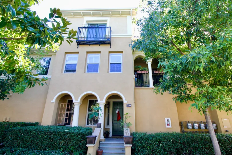 A sunny day in Garland Park with a large house with pale orange plaster in share, surrounded by tall trees and hedges.