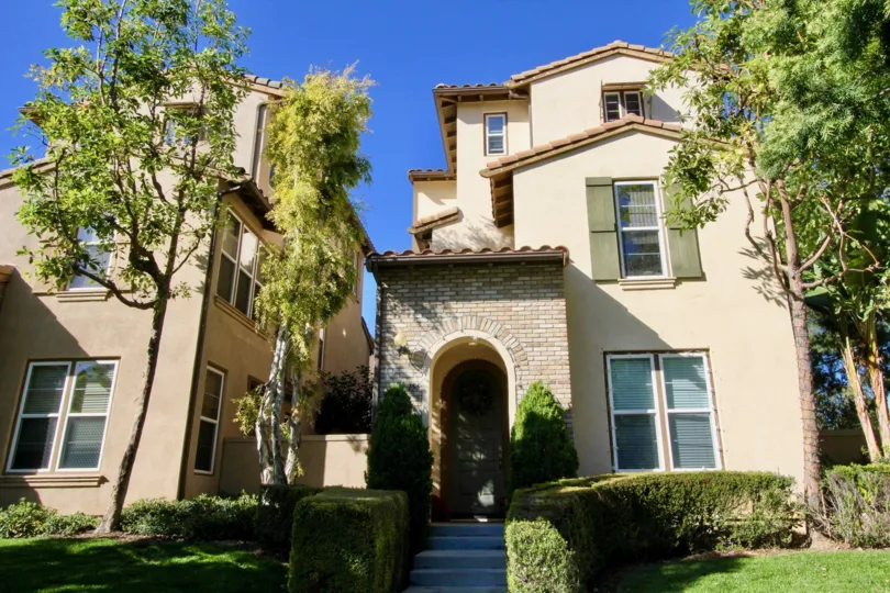 A sunny day in Ivy Wreath with a tall house with large windows and plaster and brick finish, surrounded by hedges and trees