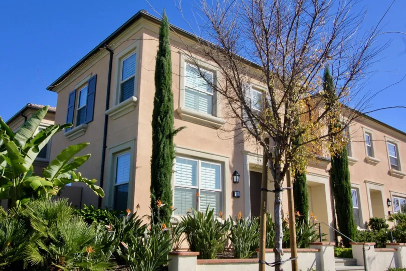 A sunny day in Jade Court with a large building with orange plaster, trees and plants.
