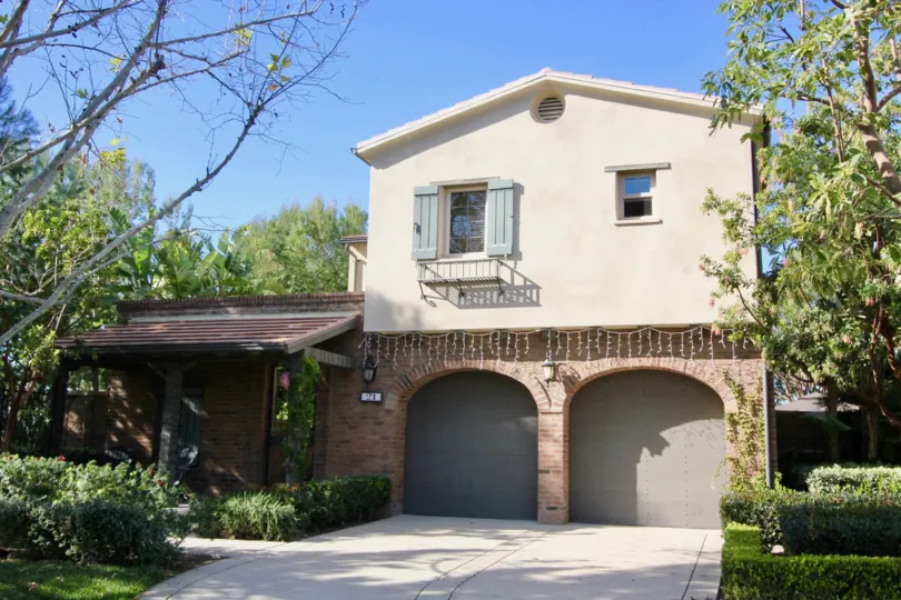 A sunny day in Los Arboles with a large house with plaster and brick finish and a garage
