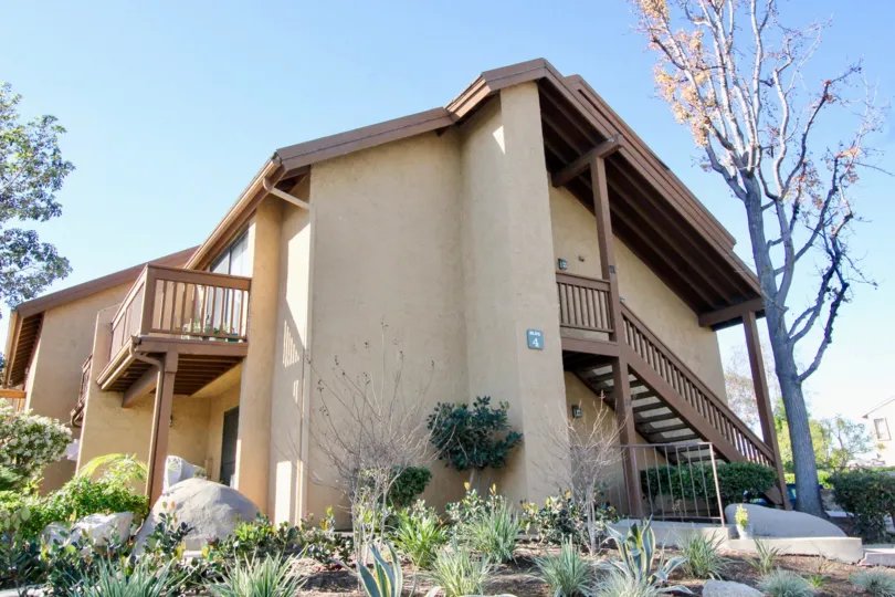 A sunny day in Orangetree Lake Condos with a large house with stairs, a balcony and tall trees