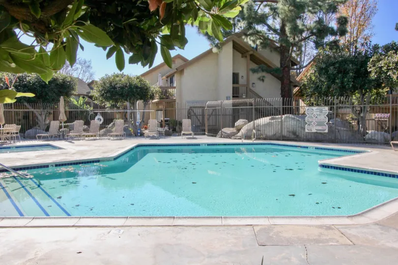 A clean pool decorated with chairs inside the compound wall near building decorated with trees and plants in Orangetree Lake Condos