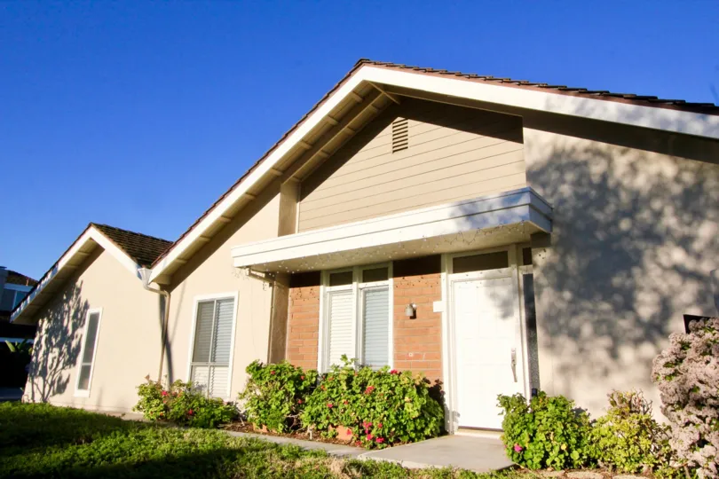 A sunny day in Park Homes with a large bungalow with plaster and brick finish and some plants in the yard
