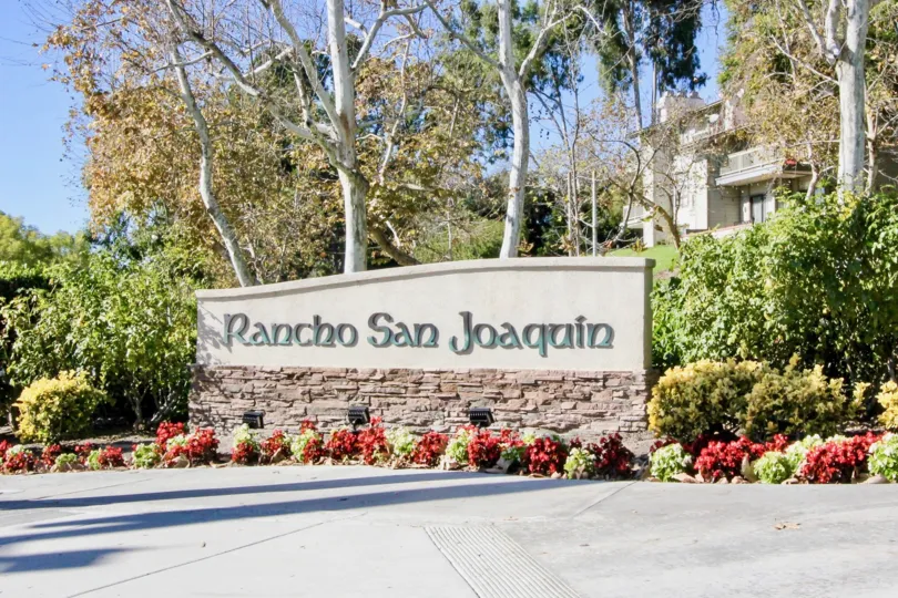 Townhome complex sign with bushes and trees and building in the background