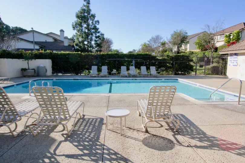 THIS IMAGE VIEWS THE BEAUTIFUL SWIMMINGPOOL WHICH HAS LOT OF CHAIRS, AND SHOWS THE MANY PLANTS AND TREES IN THE IRVINE CITY