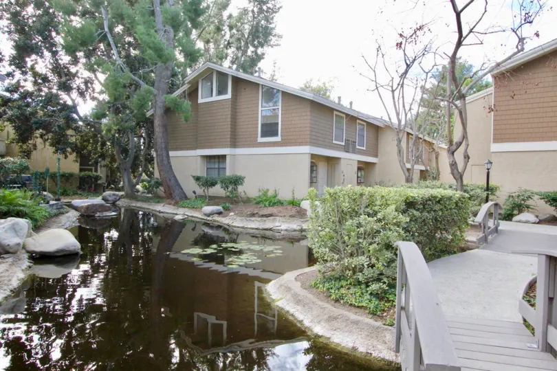 Overcast view of small pond with rocks and apartment buildings at The Lakes in Irvine, California