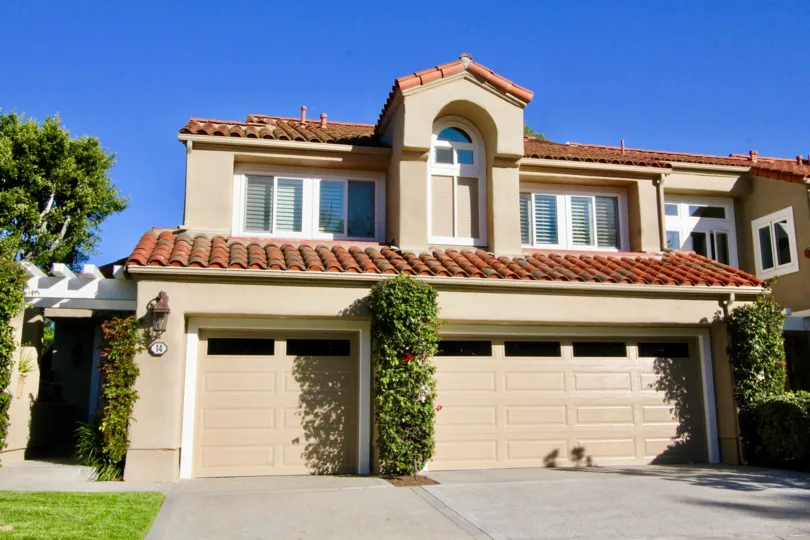 a sunny day in Turtle Rock Pointe with a tan home, driveway, and a few shrubs