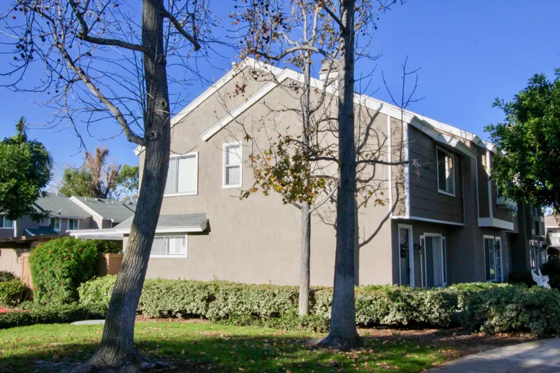 A two story gray home surrounded by shrubs and trees inside Village Glen in Irvine CA