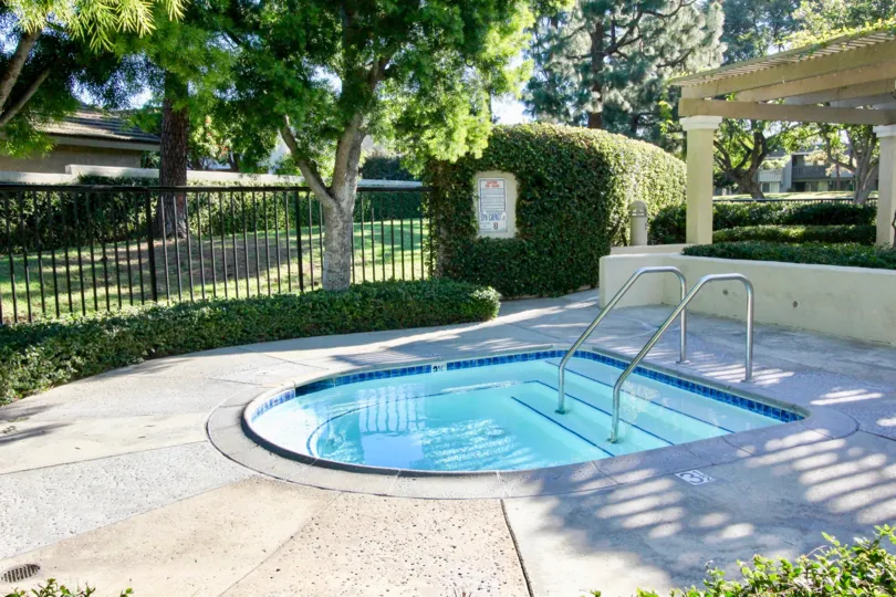 Shield shaped hot-tub behind a black iron fence inside Village Glen in Irvine CA