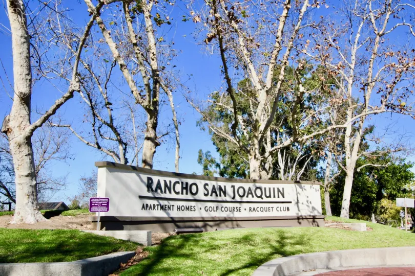 A large community sign in front of trees on a grass covered hill at Villas at RSJ in Irvine CA