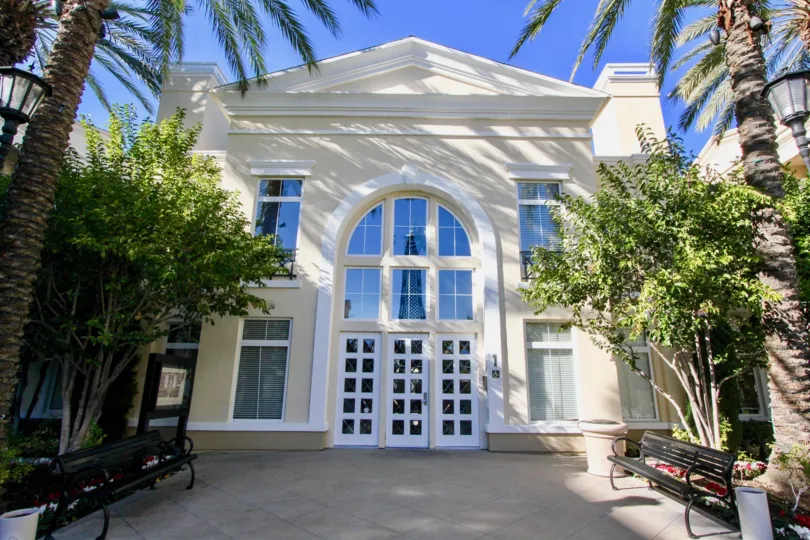 Large white building with benches and various trees out front