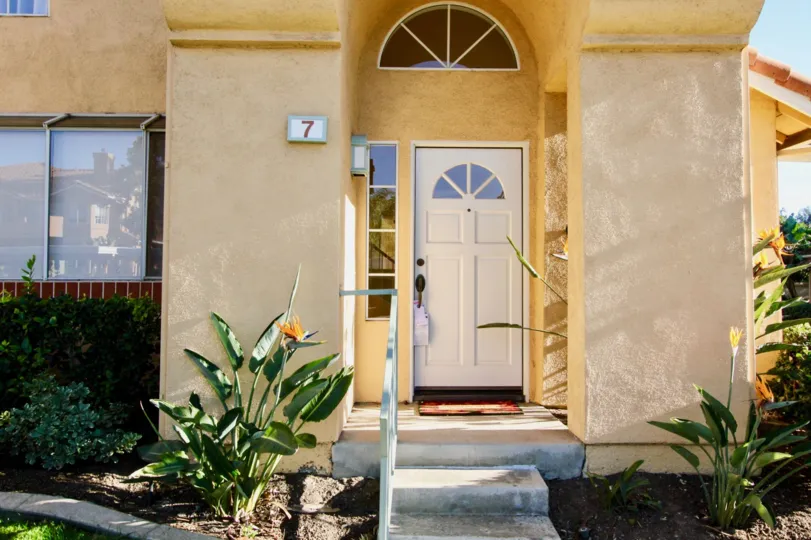 A bright yellow stucco house with a white door and the house number 7 painted on the front porch in Irvine, CA.
