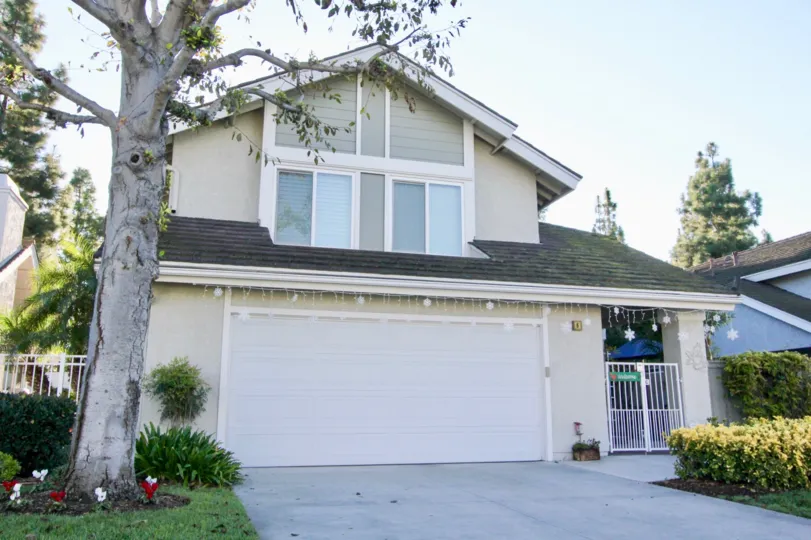 House with large tree, white gate, and garage in front