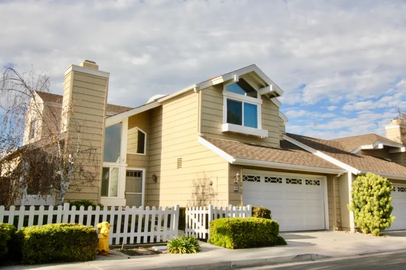 A street view of a home and garage with a white fence in Windwood Garden Homes neighborhood