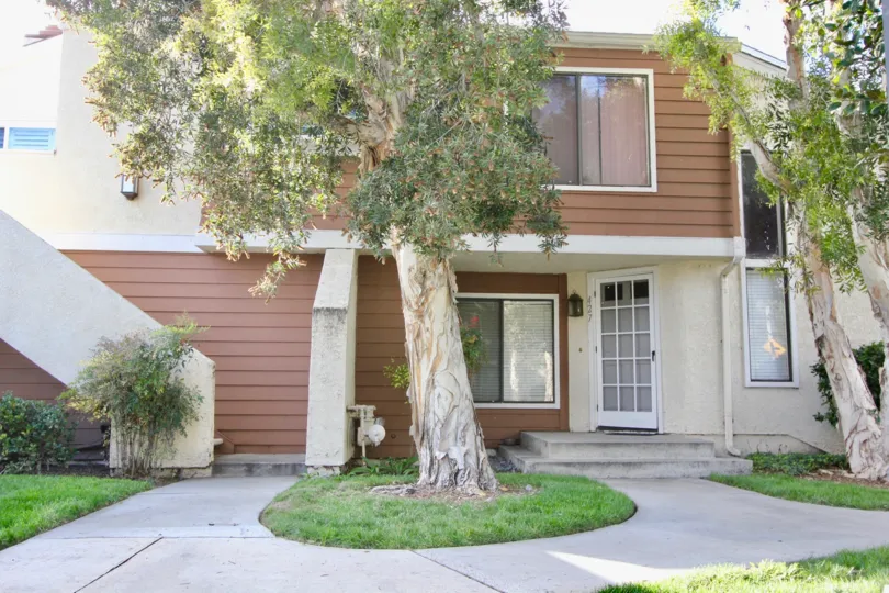 A beautiful grey and white color building in the Windwood Townhomes with some trees and lawn.