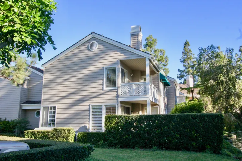 a sunny day on a complex in the Woodbridge Cove with a tall hedge, trees, and a small lawn