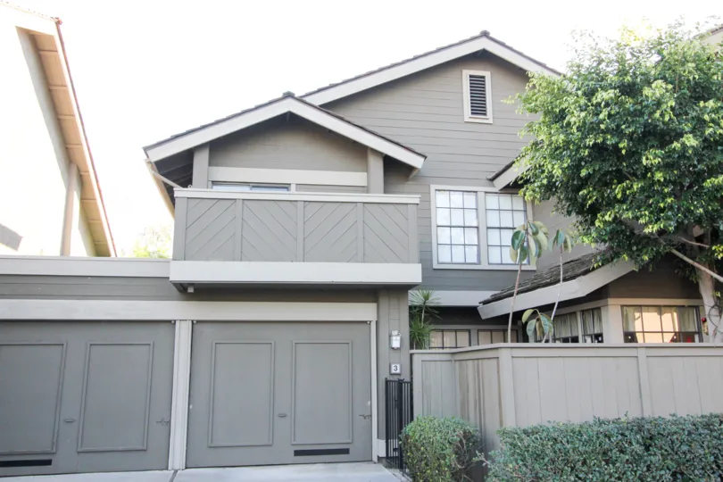 a large gray home with a garage, a tree, and shrubs in Woodbridge Crossing