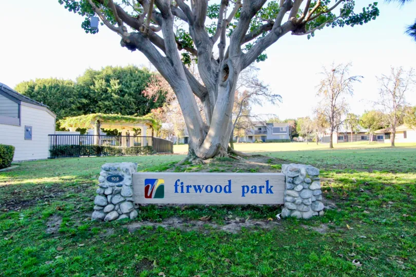 A stone and concrete signage in the Woodbridge Grove community with a large tree in the background.