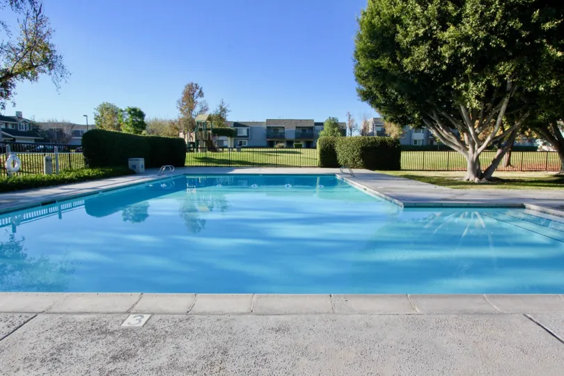 A large gated pool surrounded by grass, trees, and apartment buildings