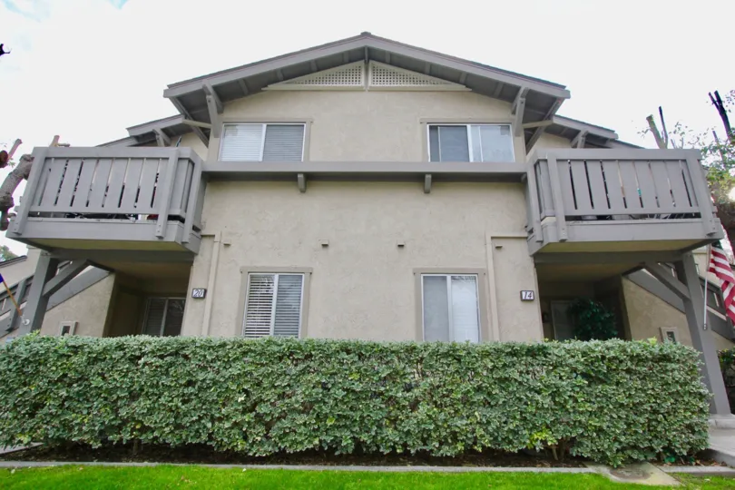 A large green hedge below a two story gray condominium at Woodbridge Reserve in Irvine CA