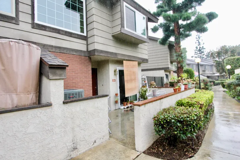 THE BUILDING IN THE LA HABRA WOODS TOWNHOMES WITH THE FLOWER POTS, PATHWAY, PLANTS, TREES