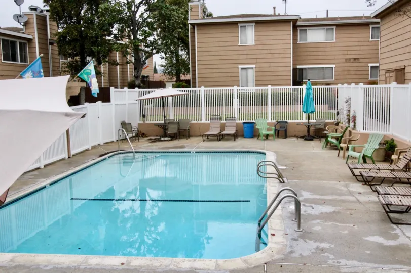 THIS IMAGE SHOWS THE SWIMMING POOL WITH LOT OF CHAIRS BACKSIDE VILLAS, LEFT SIDE FLAGS, UMBRELLA ARE VISIBLE IN IMAGE IN LA HABRA CITY