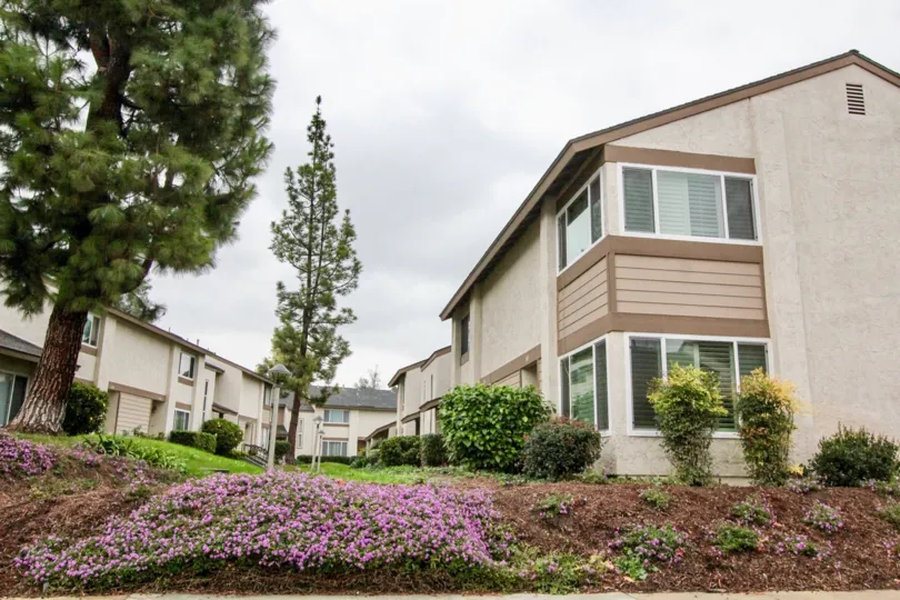 Opposite to the house in Sunny Hills Village has tall trees over the house with flowers in bushes
