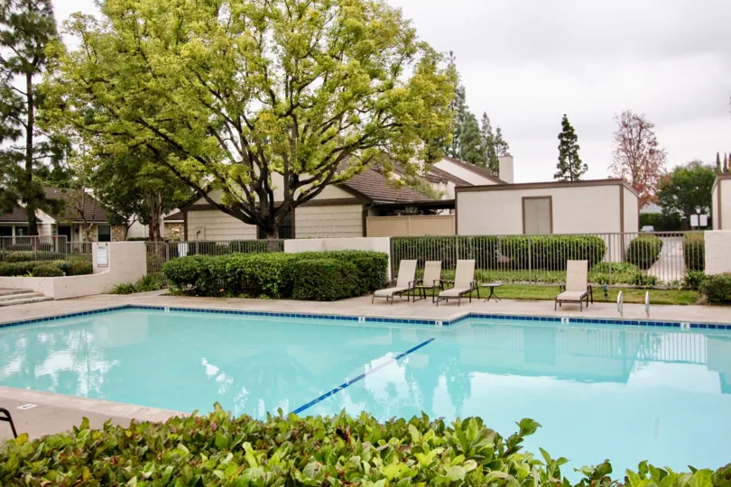 Swimming pool is in The Gables with seating chairs, trees and cutted bushes