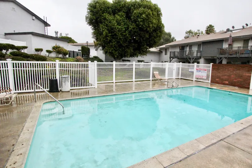THIS IMAGE SHOWS THE SWIMMING POOL IN LA HABRA THAT HAVE THE CHAIRS, ON THE LEFT SIDE PLANTS AND TREES ARE THERE