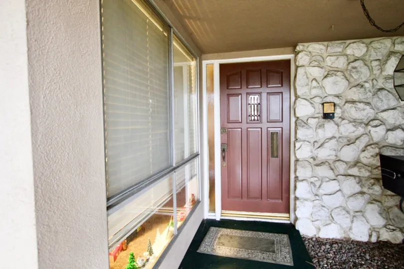 In front of a wooden door at Woodridge Townhouse with rock wall.
