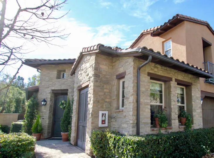 A mostly sunny day by a Castellina brick house with bushes and potted plants around it