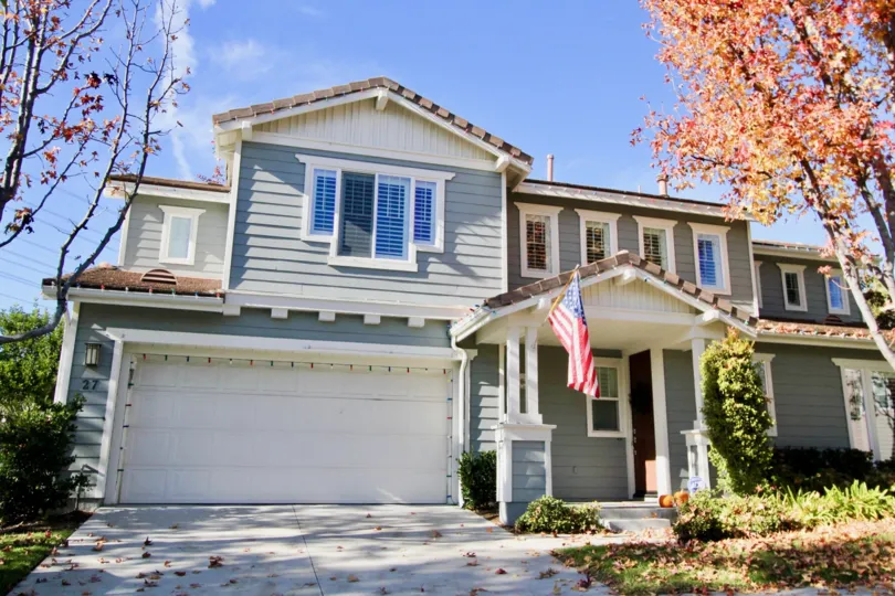 A sunny day at a Potters Bend house with an American flag in front of it and with leaves all over the driveway and lawn