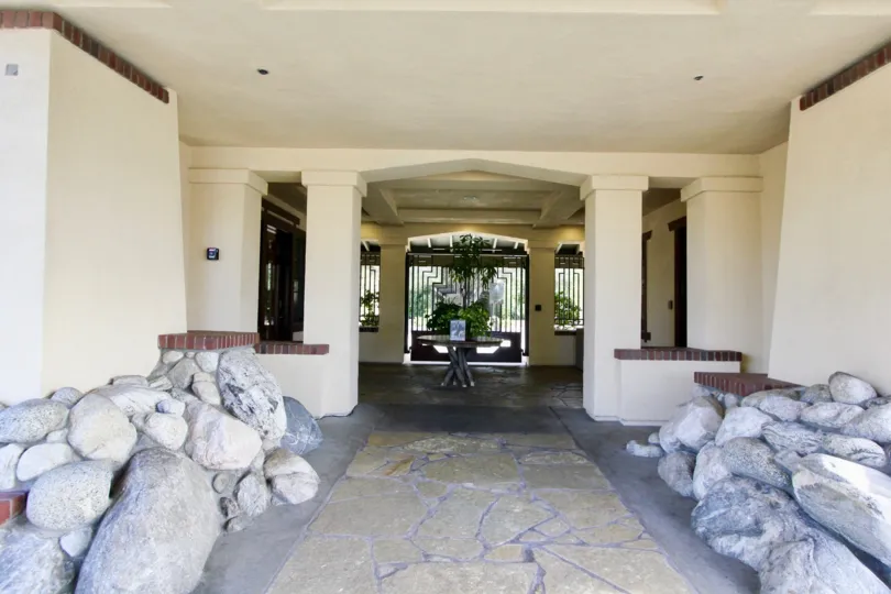A sunny day by a walkway to a building which has rock structures on both sides of it and a table at the end of the walkway